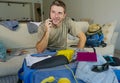 Young handsome and happy man talking with friend on mobile phone while packing travel suitcase organizing clothes and things in su Royalty Free Stock Photo