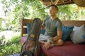 Young handsome and happy mixed ethnicity man in hipster style chilling outdoors with guitar relaxed at tranquil tropical garden Royalty Free Stock Photo