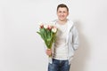 Young handsome happy smiling man student in t-shirt and light sweatshirt holds bright bouquet of white and pink tulips Royalty Free Stock Photo