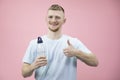 Young handsome healthy man in t-shirt holding bottle of water shows like sign