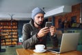 Young handsome hipster guy at the restaurant using a mobile phone. Royalty Free Stock Photo