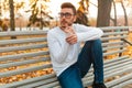 Young handsome hipster guy is sitting in autumn park on a bench. Bored alone. A student walks in the park. Royalty Free Stock Photo