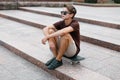 Young handsome hipster man in stylish sunglasses in stylish t-shirt in trendy shorts in sneakers resting on a skateboard Royalty Free Stock Photo