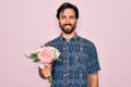 Young handsome hispanic bohemian hipster man with bear holding flowers bouquet with a happy face standing and smiling with a