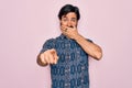 Young handsome hispanic bohemian man wearing hippie style over pink background laughing at you, pointing finger to the camera with