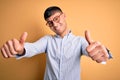 Young handsome hispanic business man wearing nerd glasses over yellow background approving doing positive gesture with hand, Royalty Free Stock Photo