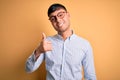 Young handsome hispanic business man wearing nerd glasses over yellow background doing happy thumbs up gesture with hand Royalty Free Stock Photo