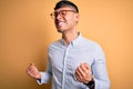 Young handsome hispanic business man wearing nerd glasses over yellow background excited for success with arms raised and eyes Royalty Free Stock Photo