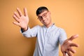 Young handsome hispanic business man wearing nerd glasses over yellow background looking at the camera smiling with open arms for Royalty Free Stock Photo