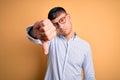 Young handsome hispanic business man wearing nerd glasses over yellow background looking unhappy and angry showing rejection and Royalty Free Stock Photo