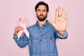 Young handsome hispanic man holding breast cancer awareness pink ribbon with open hand doing stop sign with serious and confident Royalty Free Stock Photo