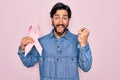 Young handsome hispanic man holding breast cancer awareness pink ribbon screaming proud and celebrating victory and success very Royalty Free Stock Photo