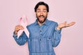 Young handsome hispanic man holding breast cancer awareness pink ribbon very happy and excited, winner expression celebrating Royalty Free Stock Photo