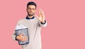 Young handsome hispanic man holding paper bin full of crumpled papers with open hand doing stop sign with serious and confident Royalty Free Stock Photo