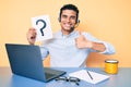 Young handsome hispanic man holding question mark as customer support smiling happy and positive, thumb up doing excellent and Royalty Free Stock Photo