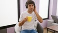 Young, handsome hispanic man joyfully enjoying his morning espresso on the sofa, at home, totally relaxed while sinking in the Royalty Free Stock Photo