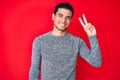 Young handsome hispanic man over red background smiling with happy face winking at the camera doing victory sign Royalty Free Stock Photo