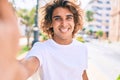 Young handsome hispanic man smiling happy making selfie by the camera at street of city