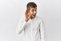 Young handsome hispanic man standing over isolated background smiling with hand over ear listening an hearing to rumor or gossip Royalty Free Stock Photo