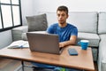 Young handsome hispanic man using laptop sitting on the floor relaxed with serious expression on face Royalty Free Stock Photo