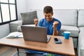 Young handsome hispanic man using laptop sitting on the floor very happy and excited doing winner gesture with arms raised, Royalty Free Stock Photo