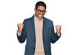 Young handsome hispanic man wearing business jacket and glasses very happy and excited doing winner gesture with arms raised, Royalty Free Stock Photo