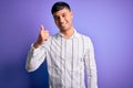 Young handsome hispanic man wearing elegant business shirt standing over purple background doing happy thumbs up gesture with hand Royalty Free Stock Photo