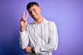 Young handsome hispanic man wearing elegant business shirt standing over purple background smiling with happy face winking at the Royalty Free Stock Photo