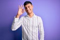 Young handsome hispanic man wearing elegant business shirt standing over purple background smiling positive doing ok sign with Royalty Free Stock Photo