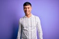 Young handsome hispanic man wearing elegant business shirt standing over purple background winking looking at the camera with sexy Royalty Free Stock Photo