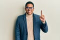 Young handsome hispanic man wearing elegant clothes and glasses showing and pointing up with finger number one while smiling Royalty Free Stock Photo