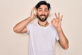 Young handsome hispanic man wearing headphones listening to music over isolated background doing ok sign with fingers, excellent Royalty Free Stock Photo