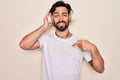 Young handsome hispanic man wearing headphones listening to music over isolated background with surprise face pointing finger to Royalty Free Stock Photo