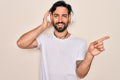 Young handsome hispanic man wearing headphones listening to music over isolated background very happy pointing with hand and Royalty Free Stock Photo