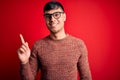 Young handsome hispanic man wearing nerd glasses over red background with a big smile on face, pointing with hand finger to the Royalty Free Stock Photo