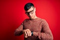Young handsome hispanic man wearing nerd glasses over red background Checking the time on wrist watch, relaxed and confident Royalty Free Stock Photo