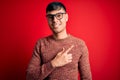Young handsome hispanic man wearing nerd glasses over red background cheerful with a smile on face pointing with hand and finger Royalty Free Stock Photo