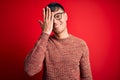 Young handsome hispanic man wearing nerd glasses over red background covering one eye with hand, confident smile on face and Royalty Free Stock Photo