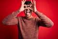 Young handsome hispanic man wearing nerd glasses over red background doing ok gesture like binoculars sticking tongue out, eyes Royalty Free Stock Photo