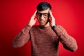 Young handsome hispanic man wearing nerd glasses over red background with hand on headache because stress Royalty Free Stock Photo