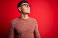 Young handsome hispanic man wearing nerd glasses over red background looking away to side with smile on face, natural expression Royalty Free Stock Photo