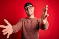 Young handsome hispanic man wearing nerd glasses over red background looking at the camera smiling with open arms for hug Royalty Free Stock Photo