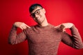 Young handsome hispanic man wearing nerd glasses over red background looking confident with smile on face, pointing oneself with Royalty Free Stock Photo