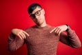 Young handsome hispanic man wearing nerd glasses over red background Pointing down looking sad and upset, indicating direction Royalty Free Stock Photo