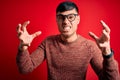 Young handsome hispanic man wearing nerd glasses over red background Shouting frustrated with rage, hands trying to strangle, Royalty Free Stock Photo