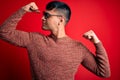 Young handsome hispanic man wearing nerd glasses over red background showing arms muscles smiling proud Royalty Free Stock Photo