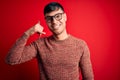 Young handsome hispanic man wearing nerd glasses over red background smiling doing phone gesture with hand and fingers like Royalty Free Stock Photo