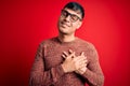 Young handsome hispanic man wearing nerd glasses over red background smiling with hands on chest with closed eyes and grateful Royalty Free Stock Photo