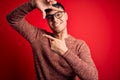 Young handsome hispanic man wearing nerd glasses over red background smiling making frame with hands and fingers with happy face Royalty Free Stock Photo