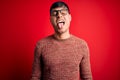 Young handsome hispanic man wearing nerd glasses over red background sticking tongue out happy with funny expression Royalty Free Stock Photo